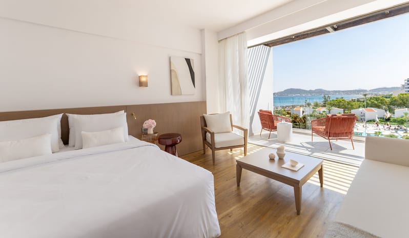 LUX ME Panoramic Guestroom Sea View Modern luxury hotel suite with white bedding, wooden floors, and a private balcony overlooking the ocean at Grecotel LUXME Dama Dama by Kenwood Travel