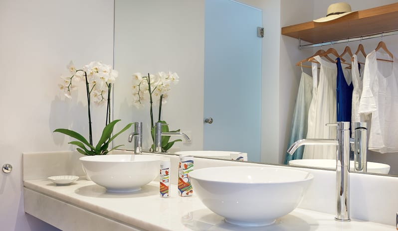 LUX ME Sea View Guestroom Bright, modern hotel bathroom vanity featuring double sinks, premium toiletries, and hanging summer vacation clothes at Grecotel LUXME Dama Dama by Kenwood Travel