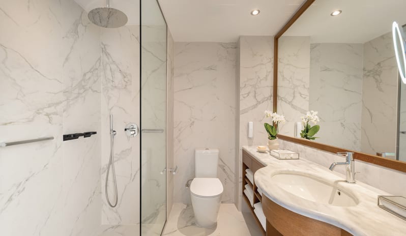 LUX ME Panoramic Guestroom Sea ViewLuxury hotel bathroom with white marble walls, a rainfall showerhead, and a large illuminated mirro at Grecotel LUXME Dama Dama by Kenwood Travel