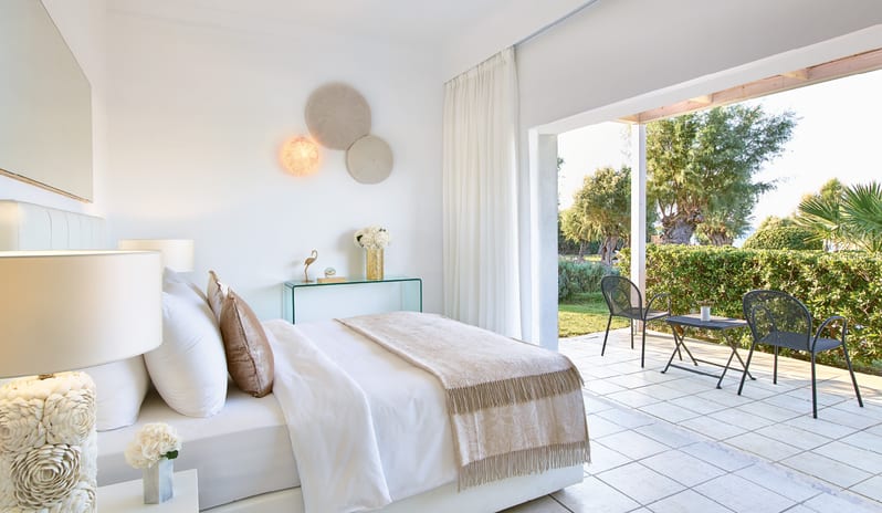Superior Bungalow Pool side white plush bed, elegant seaside decor, and a private terrace with outdoor seating overlooking lush gardens at Grecotel LUXME Dama Dama by Kenwood Travel