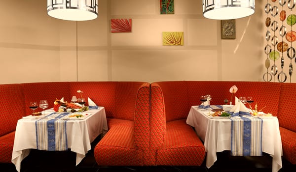 El Toro à la Carte Restaurant Close-up of elegant semi-circular red patterned booths in a luxury restaurant, featuring tables set with white linens and blue runners at Xanadu Island by Kenwood Travel