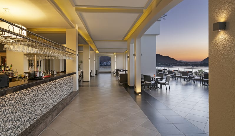Rosebud Bar & Terrace Modern luxury hotel bar and outdoor patio seating overlooking a bay at sunset with mountains in the background at Xanadu Island by Kenwood Travel
