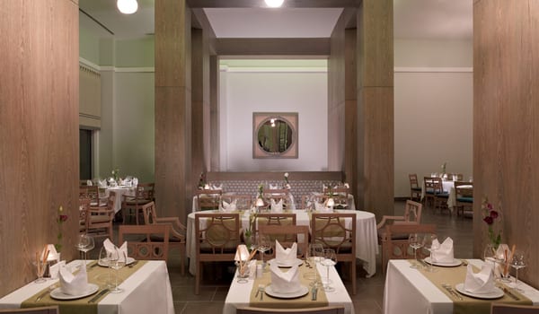 Azzurro à la Carte Restaurant high wood-paneled columns, white linen tablecloths with olive green runners, and sophisticated table settings including wine glasses and folded napkins at Xanadu Island by Kenwood Travel