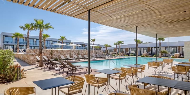 B-Llimona large turquoise swimming pool, sun loungers with white umbrellas, and a shaded patio dining area with contemporary wicker chairs under a wooden pergola at Barcelo Nura by Kenwood Travel