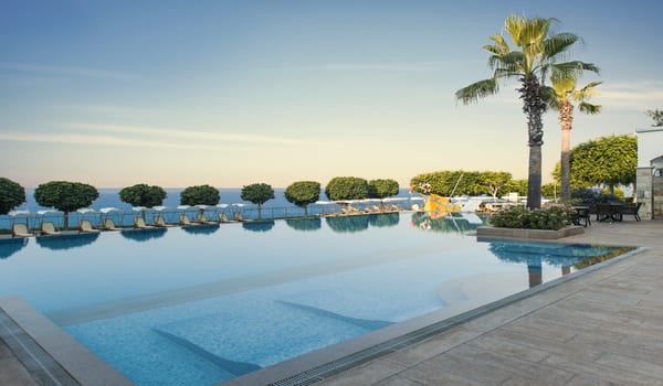 Archipelago Bar Luxury resort infinity pool overlooking the Mediterranean sea with poolside seating and tropical palm trees at Xanadu Island by Kenwood Travel