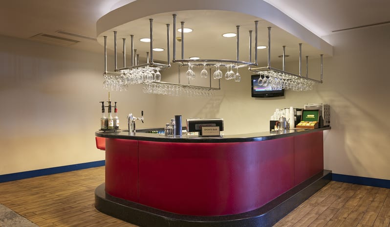 Sports Bar A modern circular sports bar with a vibrant red base, black countertop, and overhead hanging glassware rack at Xanadu Island by Kenwood Travel