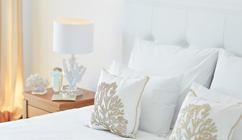 Double Guestroom Garden View white luxury bedding with gold coral embroidery and a modern coral-themed bedside lamp at Grecotel LUXME Dama Dama by Kenwood Travel