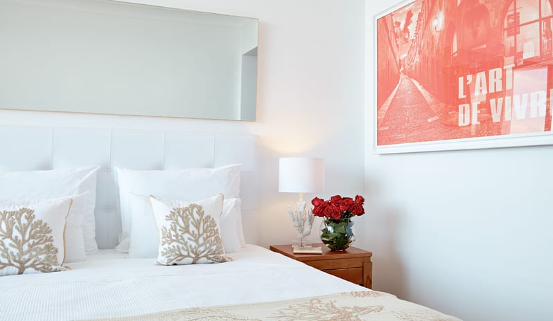 Double Guestroom Garden View white bedding with coral embroidery, red roses, and modern art at Grecotel LUXME Dama Dama by Kenwood Travel