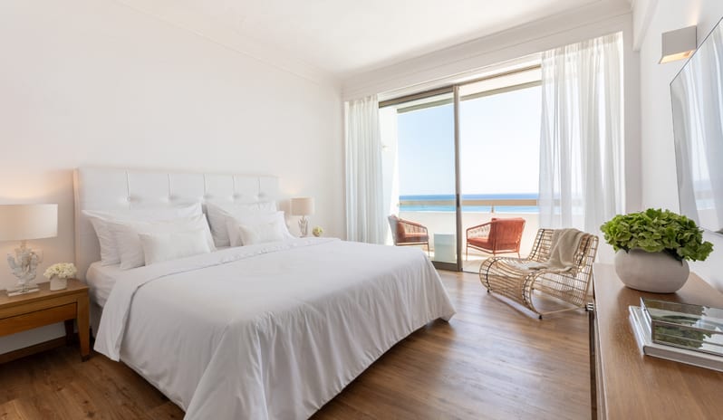 LUX ME Superior Guestroom Sea View white king-size bed, wooden flooring, and a balcony with a Mediterranean sea view at Grecotel LUXME Dama Dama by Kenwood Travel