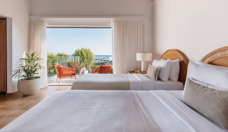 Two Bedroom Bungalow Suite Sea View twin beds with wicker headboards and a balcony view of the Mediterranean sea at Grecotel LUXME Dama Dama by Kenwood Travel