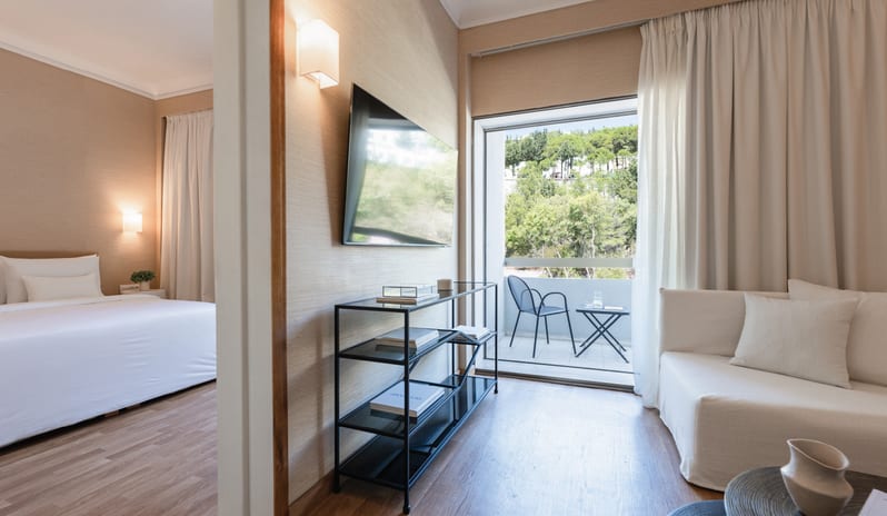 Grand Family Apartment Inland View modern bedroom, living area with sofa, and private balcony overlooking trees at Grecotel LUXME Dama Dama by Kenwood Travel
