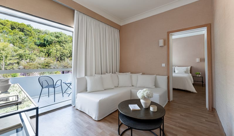 Grand Family Apartment Inland View modern bedroom, living area with sofa, and private balcony overlooking trees at Grecotel LUXME Dama Dama by Kenwood Travel