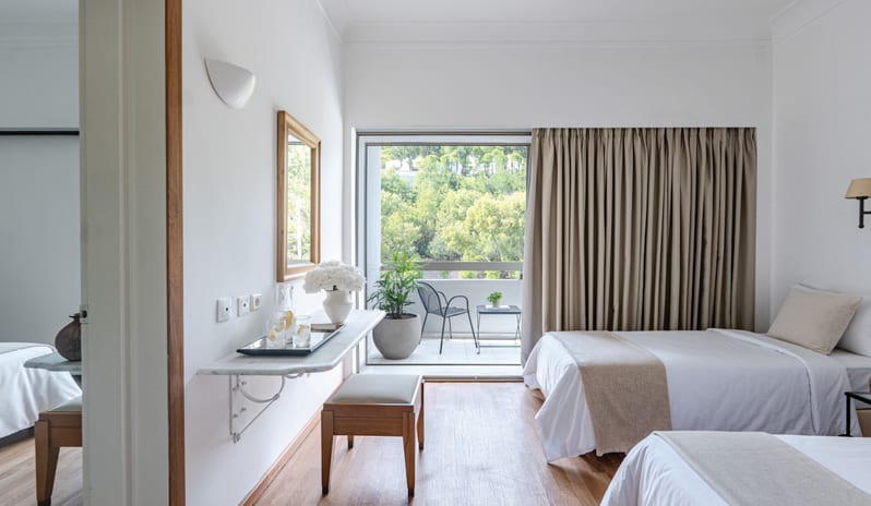 Premier Family Guestroom Inland View twin beds, a marble vanity desk, and a private balcony overlooking a lush inland forest view at Grecotel LUXME Dama Dama by Kenwood Travel
