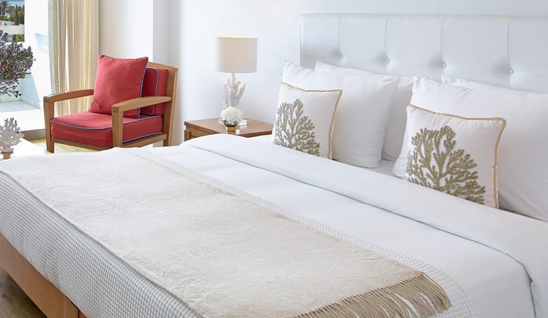 Superior Guestroom Sea View white bedding with coral-patterned pillows and a red accent chair at Grecotel LUXME Dama Dama by Kenwood Travel
