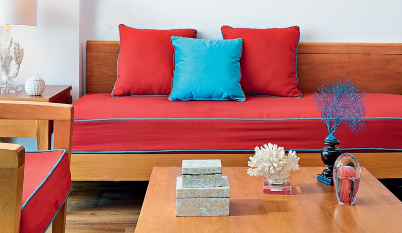 Superior Guestroom Side Sea View red sofa with turquoise cushions and coastal-themed decor including coral sculptures on a wooden coffee table at Grecotel LUXME Dama Dama by Kenwood Travel