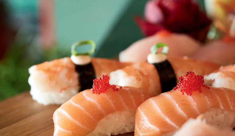 Asiana Close-up of fresh salmon and shrimp nigiri sushi topped with red tobiko, served on a wooden board at Grecotel LUXME Dama Dama by Kenwood Travel