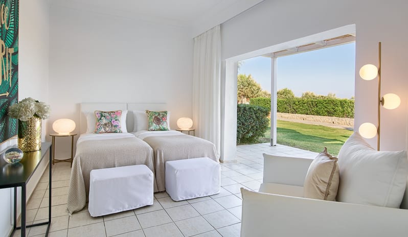 LUX ME Family Bungalow Pool side modern white decor, vibrant floral cushions, and a large sliding door opening onto a private garden terrace at Grecotel LUXME Dama Dama by Kenwood Travel