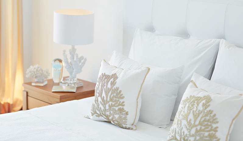Superior Guestroom Side Sea View white pillows with intricate gold coral embroidery and a coral-themed bedside lamp at Grecotel LUXME Dama Dama by Kenwood Travel