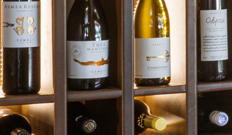 Italian à la Carte Interior detail of a luxury hotel wine cellar display featuring various bottled wines with warm accent lighting at Grecotel LUXME Dama Dama by Kenwood Travel