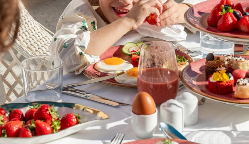 Asiana A smiling young boy enjoying a healthy breakfast with fresh strawberries and eggs at Grecotel LUXME Dama Dama by Kenwood Travel