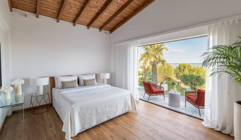 Two Bedroom Bungalow Suite Sea View large white bed, wooden vaulted ceilings, and a private balcony overlooking the sea and palm trees at Grecotel LUXME Dama Dama by Kenwood Travel