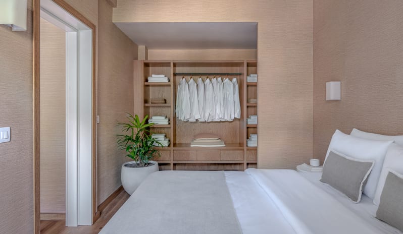 Superior Family Apartment Inland Viewlarge built-in wooden wardrobe with organized white shirts and linens, a potted plant, and a bed with neutral-toned pillows at Grecotel LUXME Dama Dama by Kenwood Travel