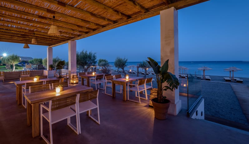 Beach Club candlelit wooden tables under a bamboo roof with a view of the beach at twilight at Grecotel LUXME Dama Dama by Kenwood Travel