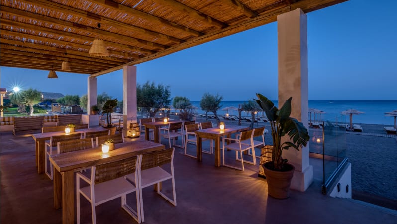 Wine Library candlelit wooden tables under a bamboo pergola at dusk with a view of the Aegean Sea at Grecotel LUXME Dama Dama by Kenwood Travel