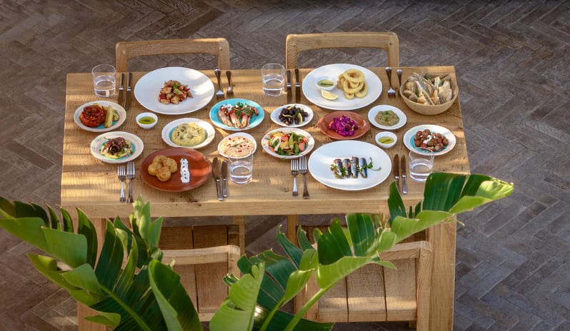 Tavernaki featuring grilled sardines, calamari, salads, and dips on a wooden outdoor table at Grecotel LUXME Dama Dama by Kenwood Travel