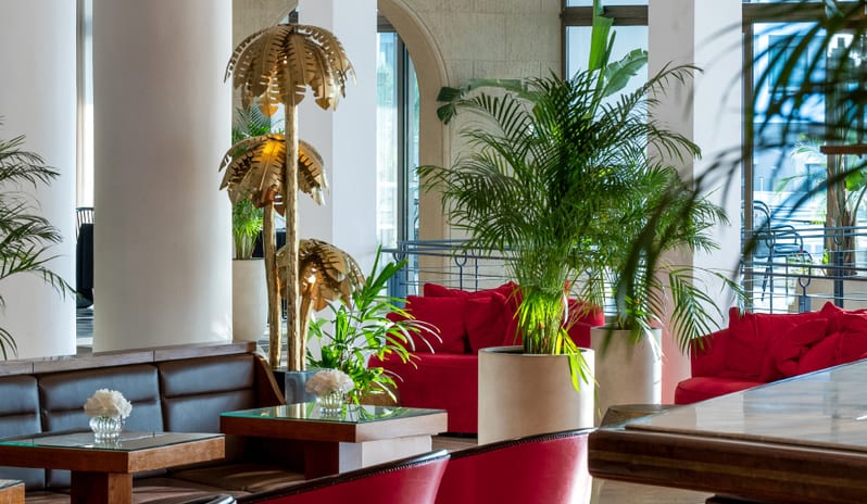 Lobby Bar chic red armchairs, leather banquette seating, and decorative gold palm tree floor lamps at Grecotel LUXME Dama Dama by Kenwood Travel