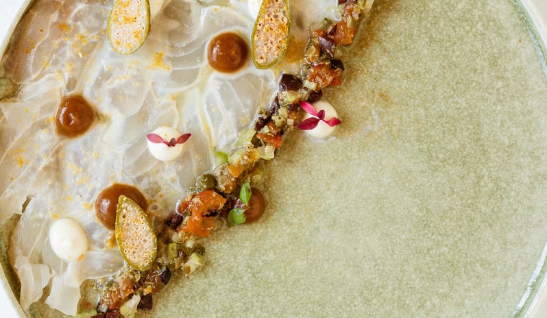 Botanica Fine Dining A beautifully plated gourmet seafood carpaccio dish garnished with caper berries, microgreens, and delicate sauces at Grecotel LUXME Costa Botanica by Kenwood Travel