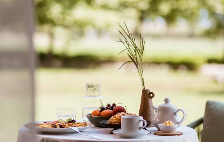 Family Apartment Private Balcony Al fresco resort breakfast setup on a sunny terrace in Corfu, featuring a gourmet morning spread with a view of lush estate groundsat Grecotel LUXME Costa Botanica by Kenwood Travel