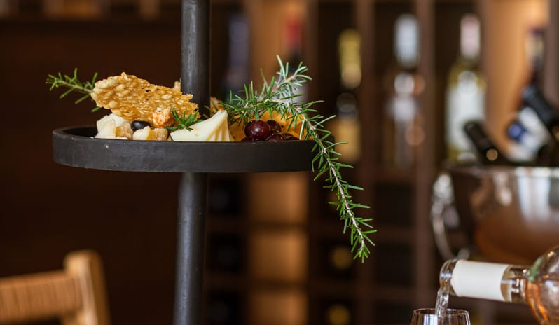 Botegga Cava di staff member presenting wine to a guest next to a fresh charcuterie platter at Grecotel LUXME Costa Botanica by Kenwood Travel