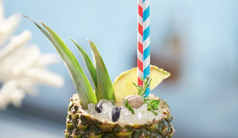 Beach Club A fresh tropical cocktail served inside a hollowed-out pineapple with crushed ice, herbs, and colorful striped straws at Grecotel LUXME Costa Botanica by Kenwood Travel