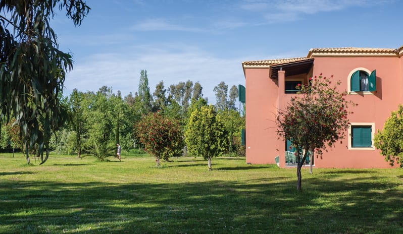 Family Apartment Veranda & GardensMediterranean resort villa building with a vast green garden estate, blooming trees, and clear blue sky at Grecotel LUXME Costa Botanica by Kenwood Travel