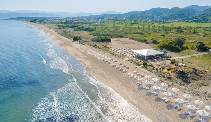 Beach Club Luxury beachfront resort club on a sandy beach in Corfu with rows of umbrellas and sunbeds next to the Mediterranean Sea at Grecotel LUXME Costa Botanica by Kenwood Travel