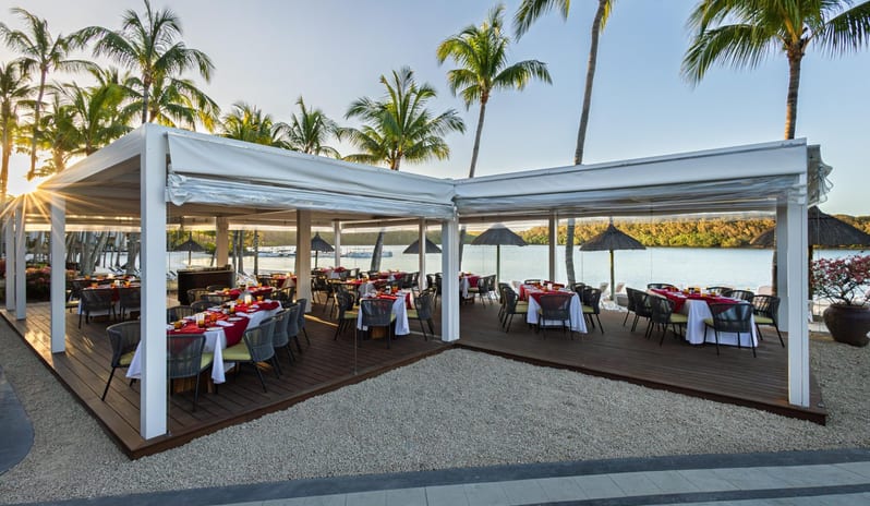 Le Grand Port Luxury resort outdoor restaurant terrace by the sea with sunset lighting and palm trees at Shandrani for 2 by Kenwood Travel
