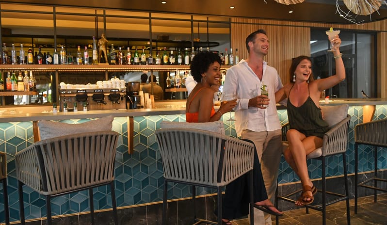 Blue Bay Bar Diverse group of friends enjoying drinks, smiling, and socializing at a modern tropical hotel lounge bar at Shandrani for 2 by Kenwood Travel