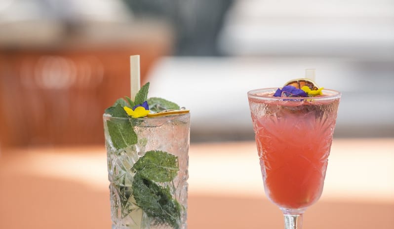 La Playa Bar A pair of refreshing craft cocktails served on a terrace table at a luxury resort, featuring fresh mint leaves and colorful floral garnishes at Shandrani for 2 by Kenwood Travel
