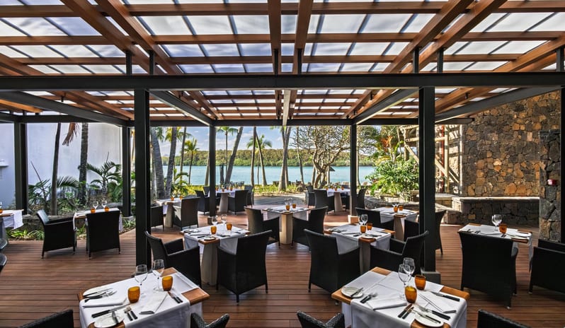 Serendipity (Adult-only restaurant) Covered restaurant patio with a modern wood and steel pergola roof canopy, stone accent walls, and neatly arranged dining tables at Shandrani for 2 by Kenwood Travel