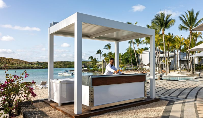 Kban bar A bartender serving tropical drinks at a modern white outdoor beach bar structure next to the ocean at a luxury resort at Shandrani for 2 by Kenwood Travel