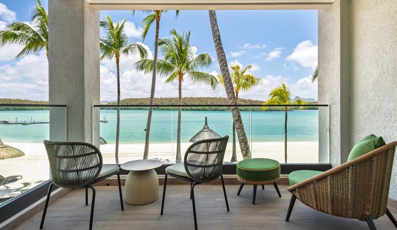 Bay View Room Scenic oceanfront balcony view of a tropical paradise beach with calm turquoise waters, palm trees, and a glass railing at Shandrani for 2 by Kenwood Travel