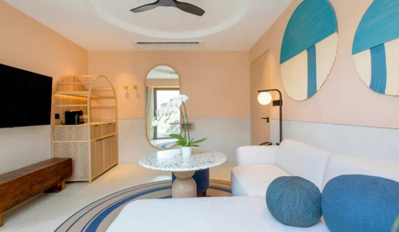 One Bedroom Private Villawhite sofa with blue accent pillows, a marble coffee table, abstract blue wall art, a large wall-mounted TV, and a wooden coffee station at Centara Karon Villas Phuket by Kenwood Travel