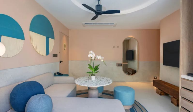 Two Bedroom Pool Villa tliving room lounge area inside a two-bedroom pool villa featuring a light gray sectional sofa, blue throw pillows, a terrazzo round coffee table with an orchid, and a wall-mounted TV at Centara Karon Villas Phuket by Kenwood Travel