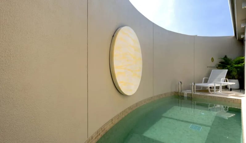 Two Bedroom Pool Villa luxury two-bedroom villa, featuring an outdoor lounge chair, a curved concrete wall with a large circular yellow art piece, and clear blue water at Centara Karon Villas Phuket by Kenwood Travel