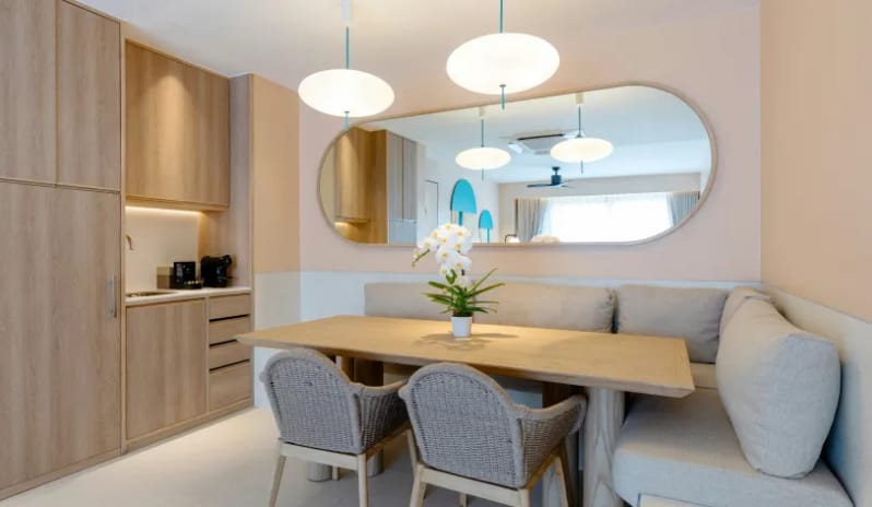 Three Bedroom Pool Villa L-shaped booth sofa, woven chairs, a large oval wall mirror, and an adjacent wooden kitchenette at Centara Karon Villas Phuket by Kenwood Travel