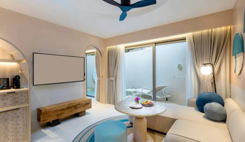 One Bedroom Pool Villa Luxury living room area of a one-bedroom pool villa, featuring a modern sofa with blue accent pillows, a round coffee table, a wall-mounted TV, and sliding glass doors to the private pool deck at Centara Karon Villas Phuket by Kenwood Travel