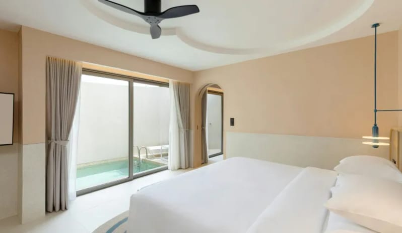One Bedroom Pool Villa Luxury bedroom inside a one-bedroom pool villa, showcasing a white plush bed, a modern blue hanging pendant light, and large sliding glass doors opening to a private plunge pool at Centara Karon Villas Phuket by Kenwood Travel