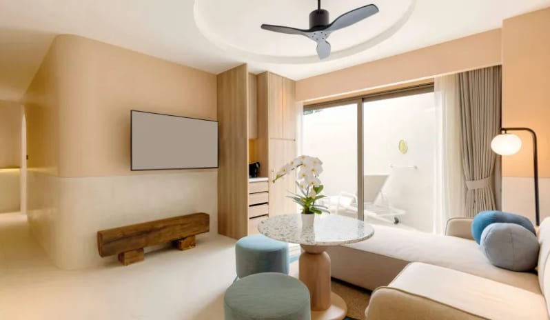 Two Bedroom Pool Villa tliving room lounge area inside a two-bedroom pool villa featuring a light gray sectional sofa, blue throw pillows, a terrazzo round coffee table with an orchid, and a wall-mounted TV at Centara Karon Villas Phuket by Kenwood Travel