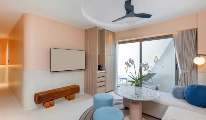 Two Bedroom Pool Villa tliving room lounge area inside a two-bedroom pool villa featuring a light gray sectional sofa, blue throw pillows, a terrazzo round coffee table with an orchid, and a wall-mounted TV at Centara Karon Villas Phuket by Kenwood Travel